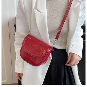 Détail du sac selle rouge brillant en cuir verni montrant la boucle argentée élégante