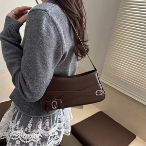 Dark brown leather shoulder bag with buckle straps shown on a model in sunlight
