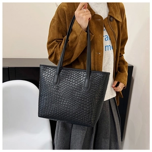 Close-up of black woven leather tote bag showing intricate texture and slim straps