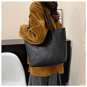 Detail shot of black woven leather tote bag texture and long shoulder strap design
