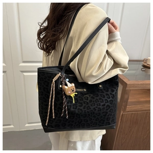 Close-up of leopard print tote bag with leather straps and cute plush bear charm accessory