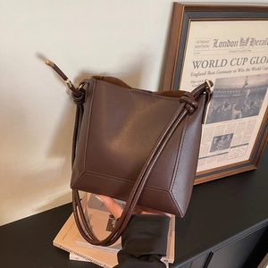 Detail of a brown leather bucket bag showing the decorative strap knots and metallic hardware