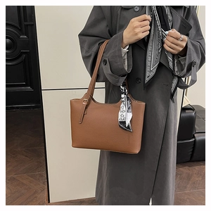 Close-up of brown lychee leather tote bag with a patterned silk scarf on strap