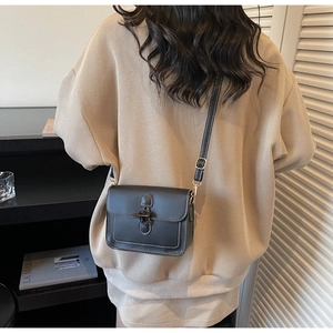 Detail of black leather crossbody bag featuring white contrast stitching and vintage clasp