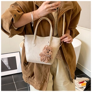 Detailed shot of an off-white bucket bag with a cute plush bear pendant and leather text