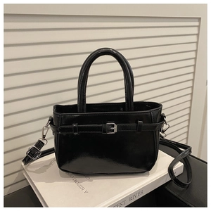 Détail du sac à main noir brillant avec boucle et sangle sur fond de livre blanc pur