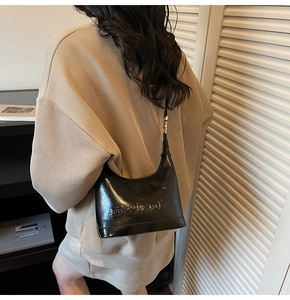 Detail view of black glossy shoulder bag with embossed letters and adjustable strap on model