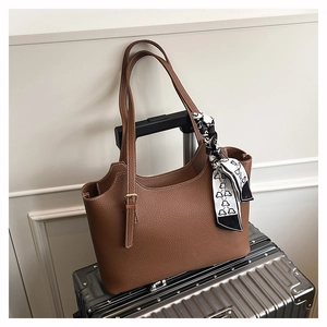 Detail of a brown leather tote bag with a patterned silk scarf on a silver travel suitcase