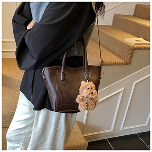 Detail of dark brown faux leather bucket bag featuring a cute plush bear charm accessory