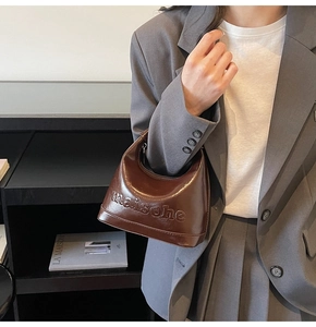 Detailed close-up of dark brown leather hobo bag with embossed letters on surface