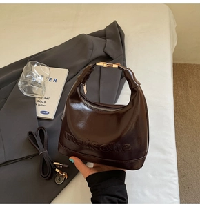 Detail of dark brown glossy croissant bag with embossed maison logo and gold metal handle