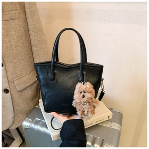 Close-up of black PU leather bucket bag with plush dog charm and detachable strap