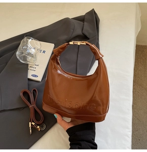 Detail of brown glossy PU leather handbag with embossed lettering and gold buckles