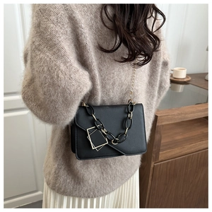 Detail of a black leather crossbody bag with dual-tone chain on a stylish model