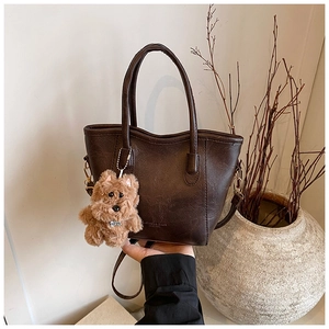 Close-up of brown faux leather bucket bag with plush dog charm and detachable strap