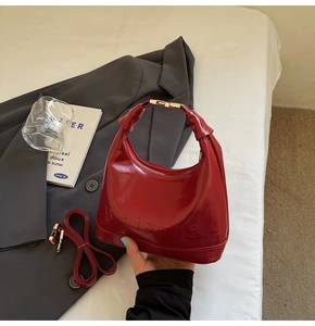 Detail view of red glossy patent leather crescent bag with embossed texture and metal strap clasp