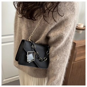 Detail of minimalist black leather crossbody bag with dual gold chain and buckle