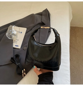 Detail view of black polished leather hobo bag with embossed letters and gold metal buckle