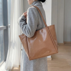 Brown patent leather tote bag detail with glossy finish shown on model's shoulder