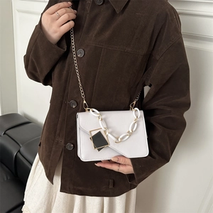 White faux leather crossbody bag with gold chain and resin strap on a female model