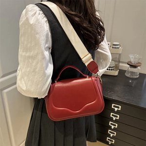 Sacoche selle en cuir PU rouge avec large bandoulière en toile et fermoir doré sur modèle