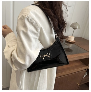 Detail of glossy black patent leather baguette bag with golden metal bow on the shoulder