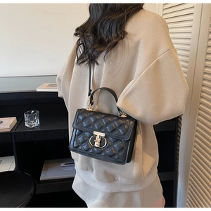 Detail of a black quilted shoulder bag with gold clasp worn by a woman in a beige sweater