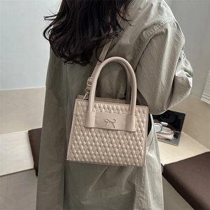 Quilted beige handbag with golden bow detail and crossbody strap worn on trench coat