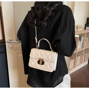 Close-up of cream quilted crossbody bag with golden metal handle and twist lock