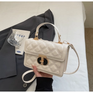 Detail of quilted beige square crossbody bag with gold metal twist lock and top handle