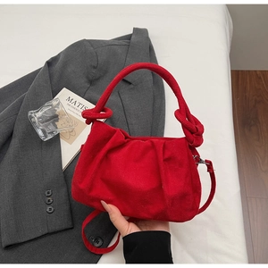 Close-up of a red pleated suede handbag with a knot handle on a white fabric surface