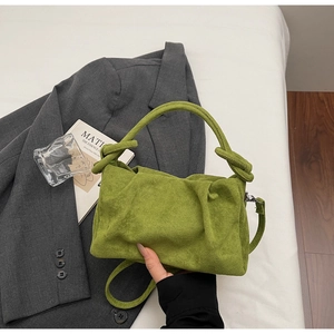 Minimalist green suede handbag with knotted handle and shoulder strap on a grey blazer