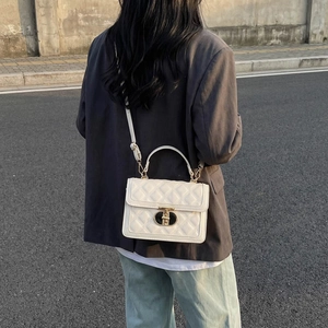 Fashionable white quilted square crossbody bag with gold lock shown in street style view