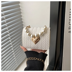 Detail of white woven crossbody bag with gold heart clasp and pearl handle