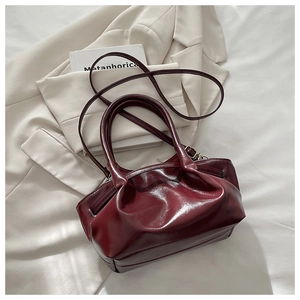 Detail of burgundy ruched bucket bag with gold hardware on white fabric background