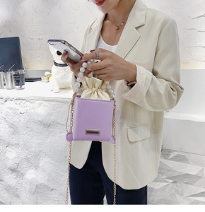 Detail of purple square box bag featuring oversized pearl handle and gold chain strap
