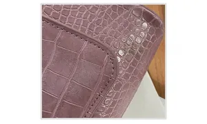 Detailopname van de gelijkmatige stiksels op de paarse schoudertas met krokodillentextuur