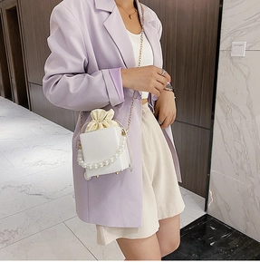 Detail of white box handbag featuring pearl handle and beige drawstring pouch