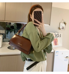 Detailed close-up of brown leather baguette shoulder bag with gold brand lettering