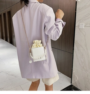 Elegant white square crossbody bag with pearl handle and metal chain on a lavender blazer
