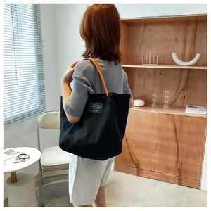 Borsa tote in tela nera con manici in pelle e toppa verde indossata a spalla