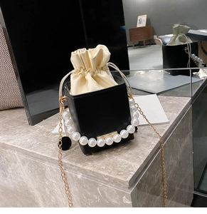 Detail of black leather bucket bag with large pearl handle and metal chain strap
