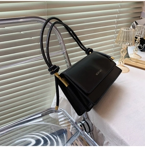 Detail of black rectangular baguette bag with gold hardware and knotted shoulder strap