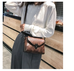 Detail of vintage brown leather crossbody bag featuring a retro metal buckle on a flap cover