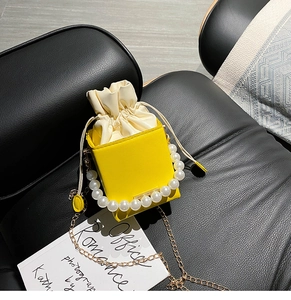 Detail of yellow mini bag with pearl handle and golden chain on leather surface
