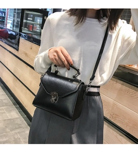 Close-up of black retro style handbag with round metal swivel lock and adjustable strap