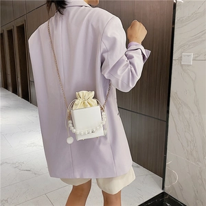Elegant white square crossbody bag with pearl handle and gold chain on lavender suit