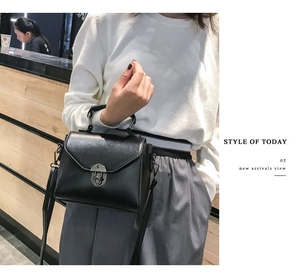 Detail view of black textured handbag featuring a vintage silver clasp and top handle