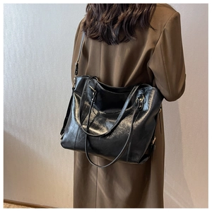 Détail d'un grand sac cabas en cuir noir brillant porté à l'épaule par un mannequin chic