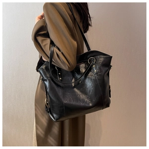 Détail du sac cabas en cuir noir brillant avec finitions dorées et texture plissée chic